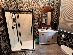 A bathroom with a glass shower enclosure, a sink with a mirror above it, and a toilet.