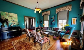 A living room with a piano, a sofa, a patterned rug, and a chandelier.