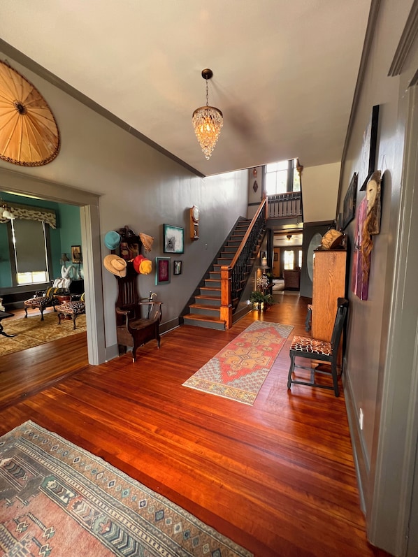 A spacious living area with hardwood flooring, a staircase, and a chandelier.