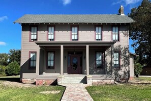 A two-story house with a front porch, a central entrance, and a brick foundation.