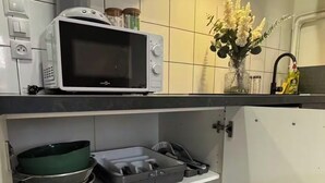 Una cocina con armarios blancos, microondas, escurreplatos y una pequeña planta.