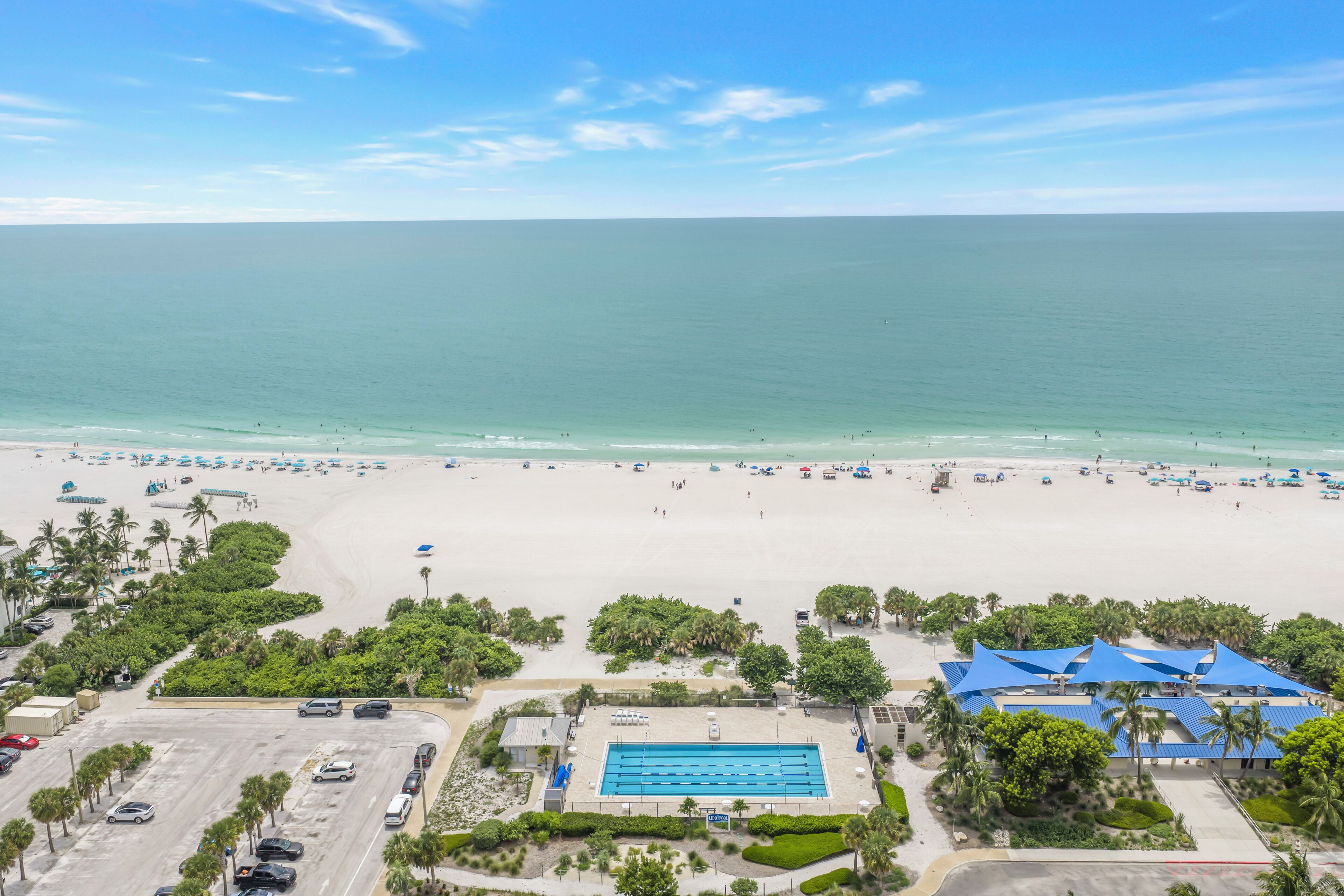 A beach resort with a swimming pool, beach umbrellas, and palm trees.
