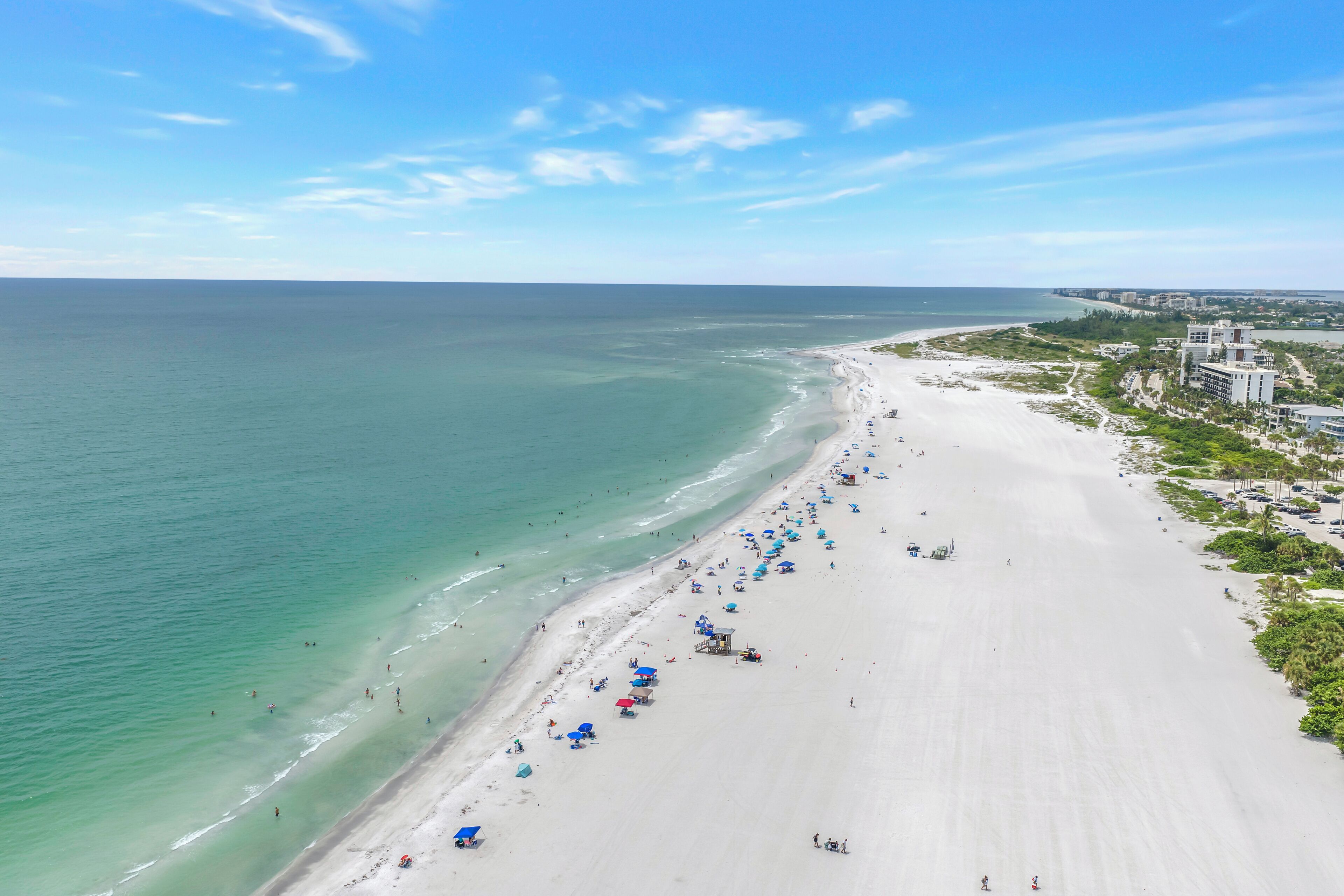 A wide beach with clear waters, a long stretch of sand, and a few umbrellas.