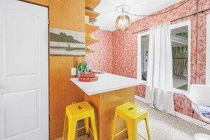 A kitchen with a white countertop, yellow stools, a hanging light fixture, and a wall with a floral pattern. - Sunny Lido Beach Studio (Sarasota)