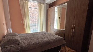 Un dormitorio con cama, armario y ventana con cortinas.