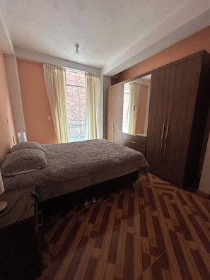 A bedroom with a bed, a wardrobe, and a window with curtains.