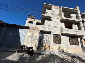 Un edificio de varios pisos con fachada de concreto, una motocicleta estacionada frente a él y un cielo azul despejado.