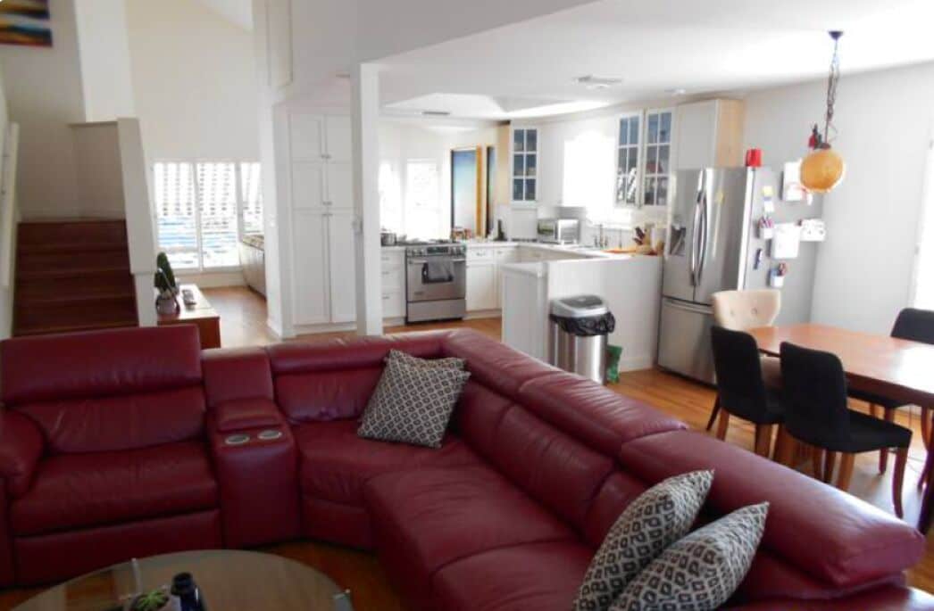 Uma sala de estar moderna com um sofá de couro vermelho, um espaço de refeições com mesa e cadeiras de madeira, e uma cozinha com armários brancos e eletrodomésticos de aço inoxidável.