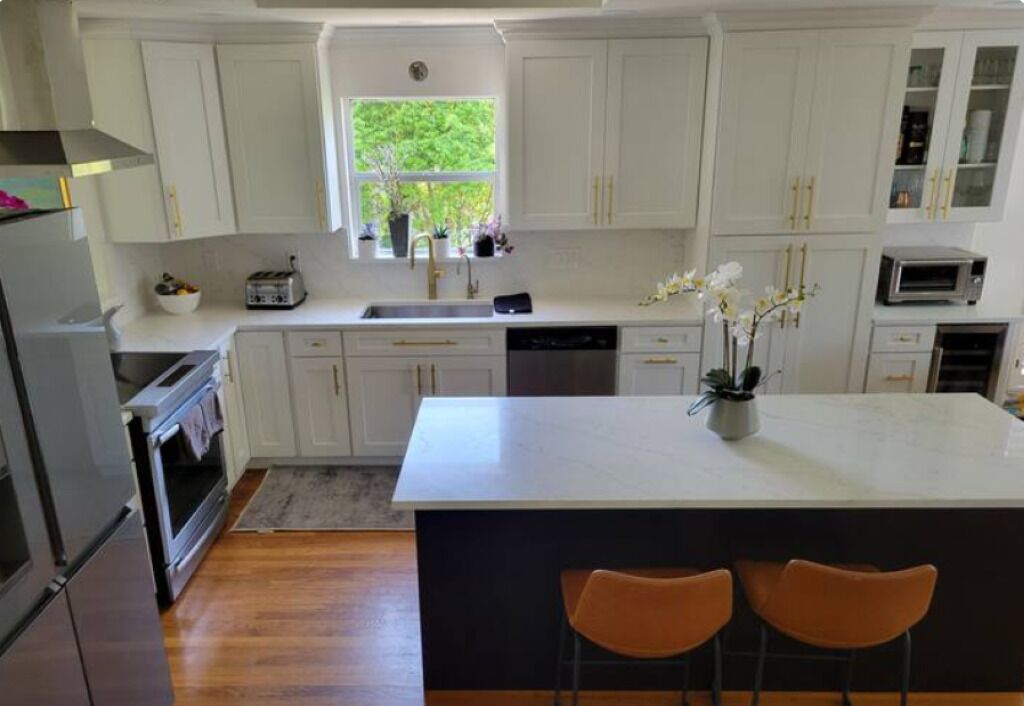 Een moderne keuken met witte kasten, een centraal eiland en twee barkrukken.