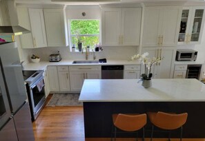 Een moderne keuken met witte kasten, een centraal eiland en twee barkrukken.