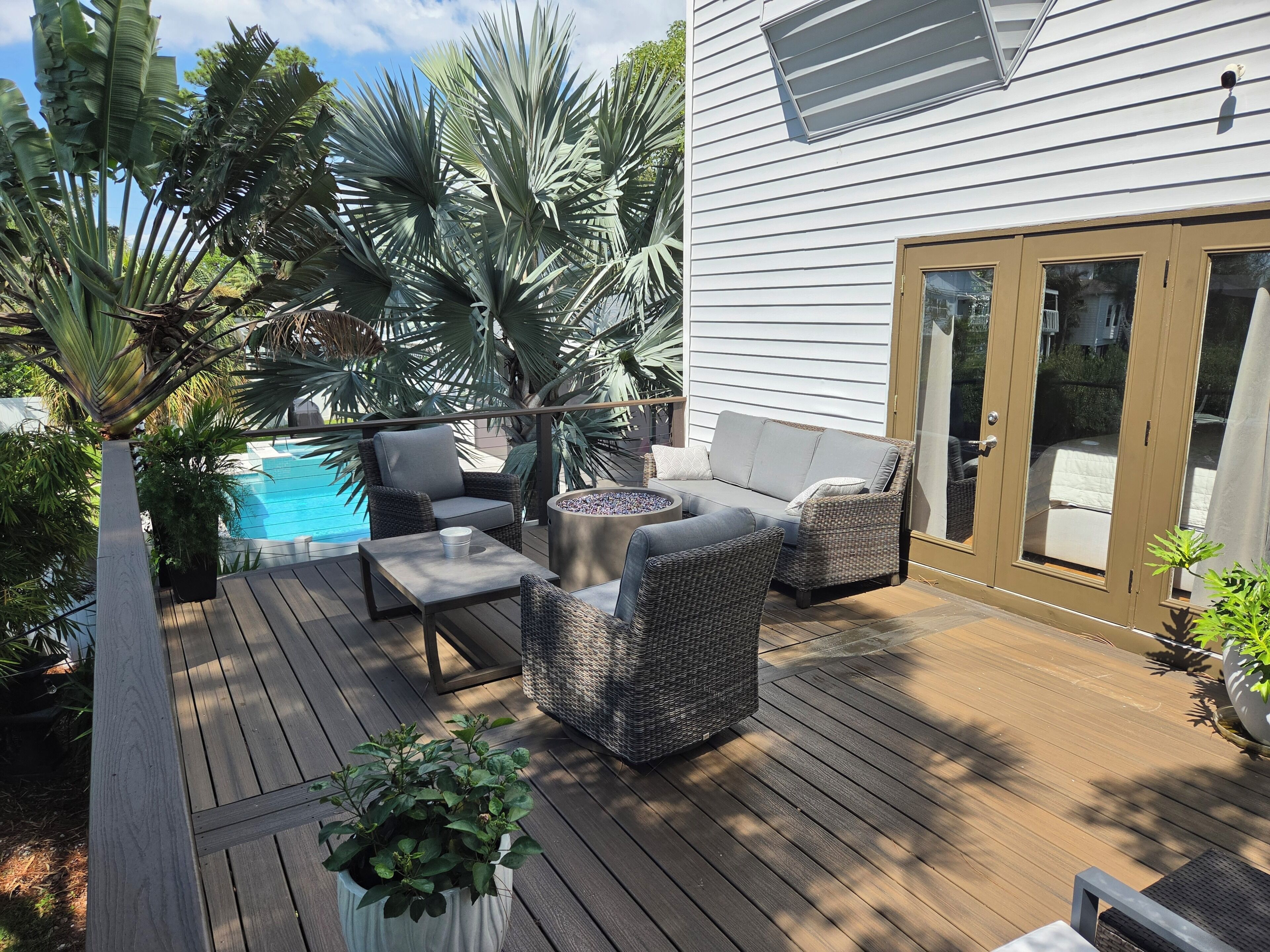 A wooden deck with outdoor furniture, a pool, and tropical plants.