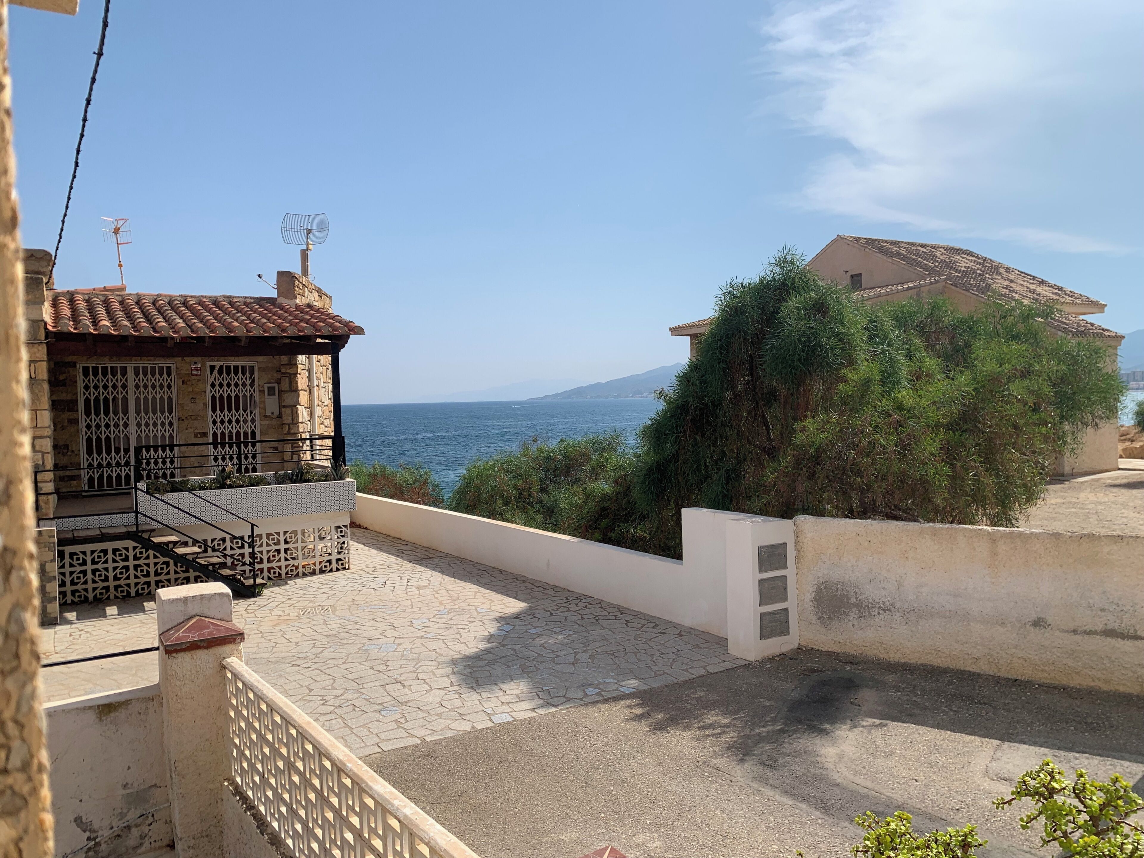 Un quartier résidentiel doté d’une terrasse dallée, d’un bâtiment en pierre avec un toit en tuiles et offrant une vue sur la mer.