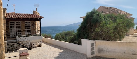 Un barrio residencial con un patio empedrado, un edificio de piedra con tejado de baldosas y vista al mar.