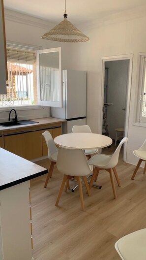 Una cocina moderna con una mesa redonda de comedor, sillas blancas, una lámpara colgante y un refrigerador.