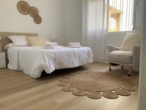 Un dormitorio con cama, una silla y un tapete tejido en el suelo.