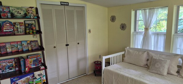 A room with a bed, a shelf with children's books and toys, a closet, and a window with curtains.