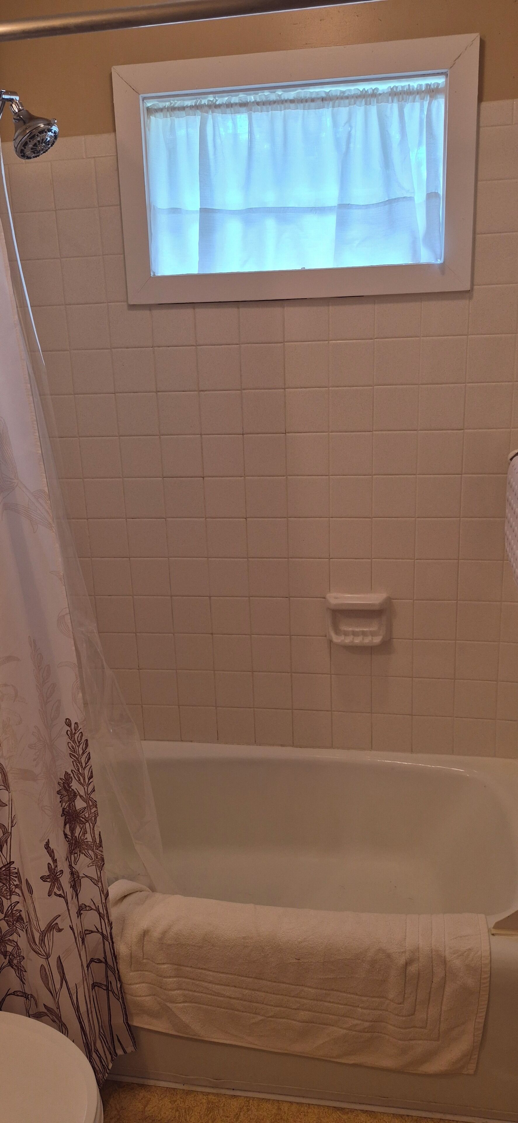 A bathroom with a bathtub, a shower curtain, a window with curtains, and a towel rack.