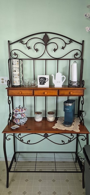 A metal-framed shelf with a mug holder, a teapot, and a coffee maker on a wooden table.