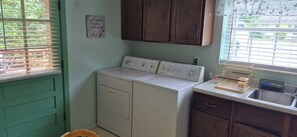 A laundry room with two white washing machines, a wooden cabinet, a sink, and a window with blinds.