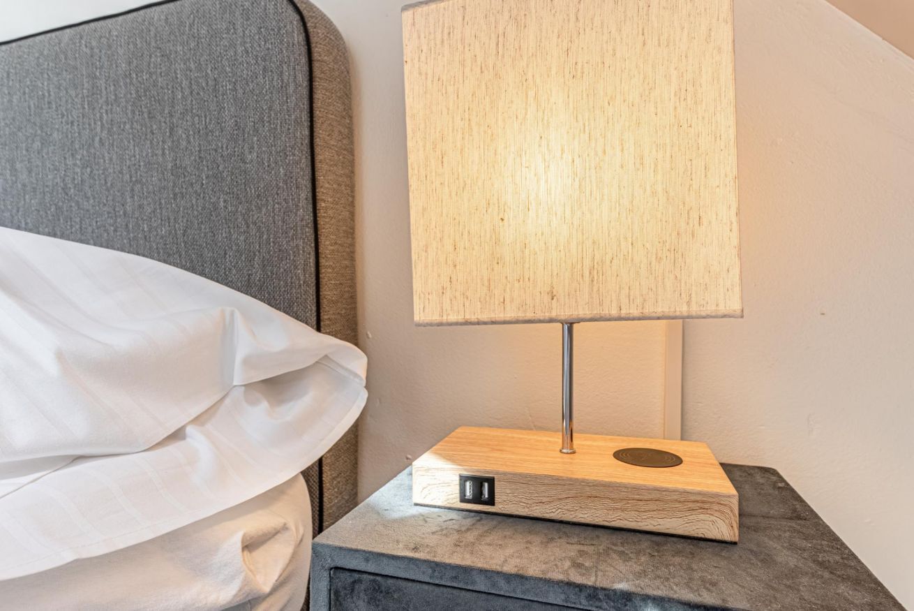 A bed with a white sheet and a wooden bedside table with a lamp.
