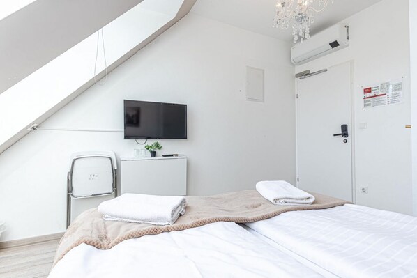 Habitación de hotel moderna con cama, televisor, escritorio con planta, puerta blanca y tragaluz.