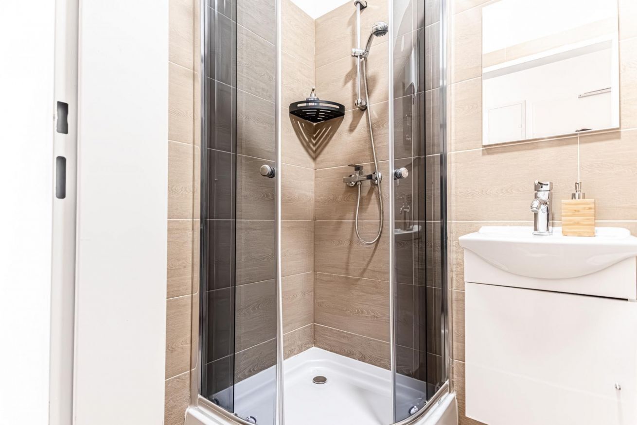 Ein modernes Badezimmer mit einer gläsernen Duschkabine, einem weißen Waschbecken und einer Holzkosmetikbank.