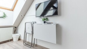 A modern, minimalistic room with a white radiator, a white desk, a mounted television, and a small potted plant.
