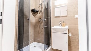 A modern bathroom with a glass-enclosed shower, a white sink, and a wooden vanity.