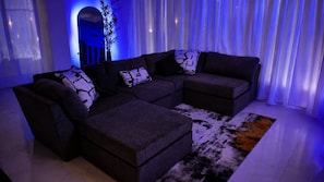 A modern living room with a sectional sofa, ottoman, and a patterned rug.