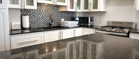 A kitchen with white cabinets, a black countertop, a microwave, and a stove.