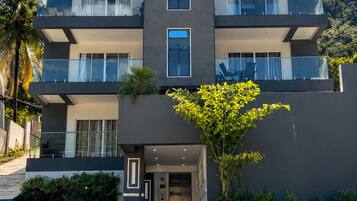 A multi-story hotel with a modern design, featuring balconies, a central entrance, and a well-maintained garden area.
