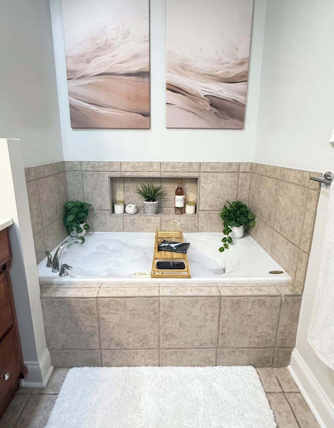 A bathroom with a large bathtub, a wooden tray, and two potted plants.