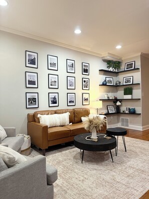 A living room with a brown sofa, a grey armchair, a black coffee table, and a patterned rug. - Cozy Canton Stay (Baltimore)