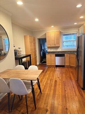 A compact kitchen with wooden cabinets, a refrigerator, and a dining area with a table and chairs. - Cozy Canton Stay (Baltimore)