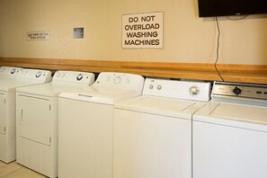 A laundry area with multiple washing machines and a sign warning against overloading them. - Dolphin Beach Club - 1 Bedroom Condo (Daytona Beach Shores)