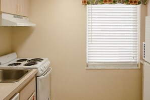 A kitchen with a stove, sink, and a window with blinds. - Dolphin Beach Club - 1 Bedroom Condo (Daytona Beach Shores)