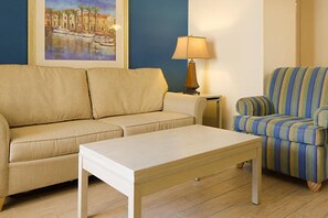 Ein Wohnzimmer mit einem beigen Sofa, einem gestreiften Sessel, einem weißen Couchtisch, einer Lampe und einem gerahmten Bild an der Wand.