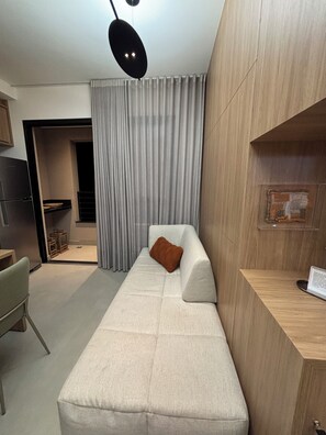A modern living room with a sofa, a wooden sideboard, a dining area, and a kitchen visible through an open door.