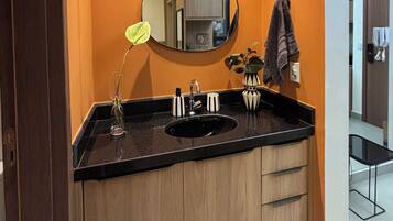 A bathroom with a black countertop, a round mirror, and wooden cabinets.