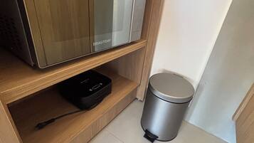 A kitchen area with a microwave, a trash bin, and a power strip on a wooden shelf.