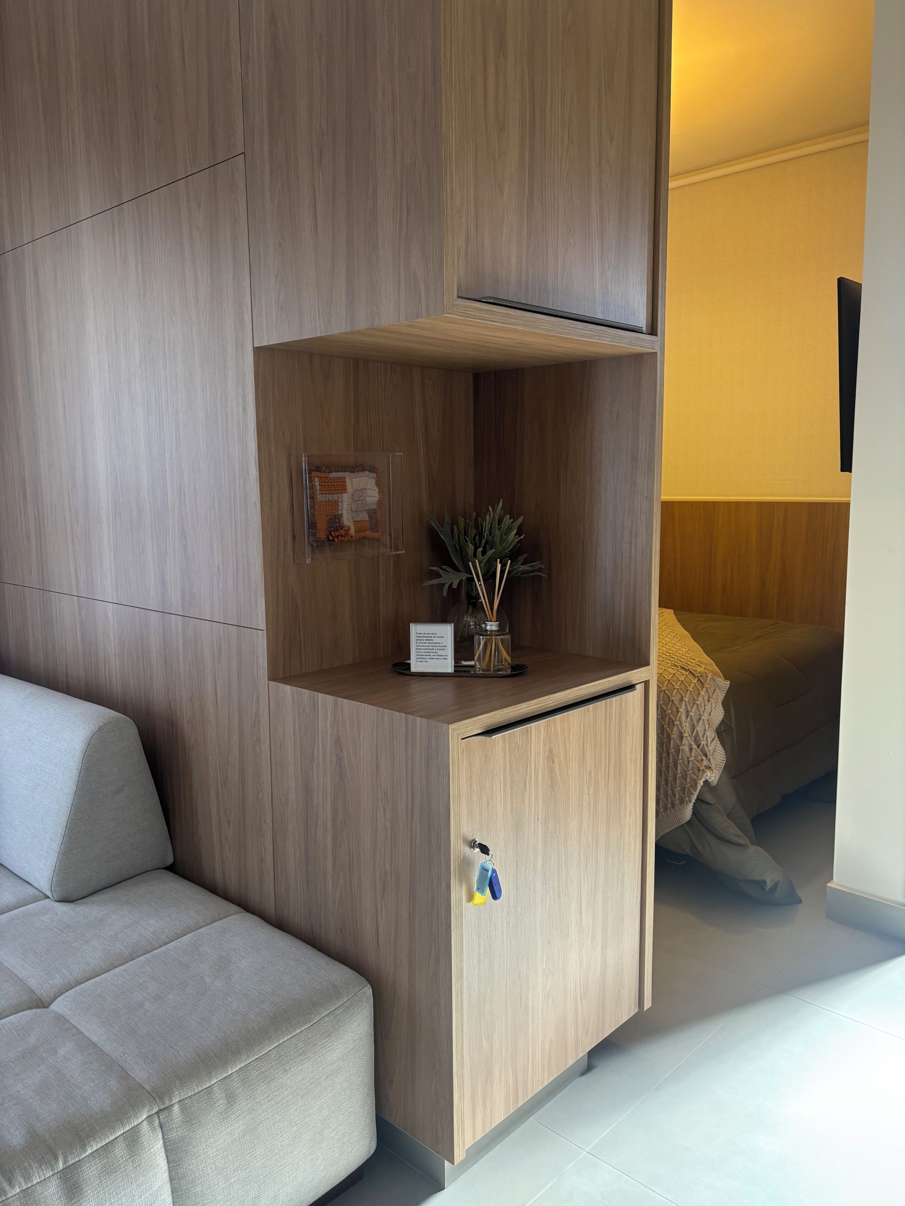 Una habitación moderna con un armario empotrado de madera, una planta pequeña y una cama con manta.