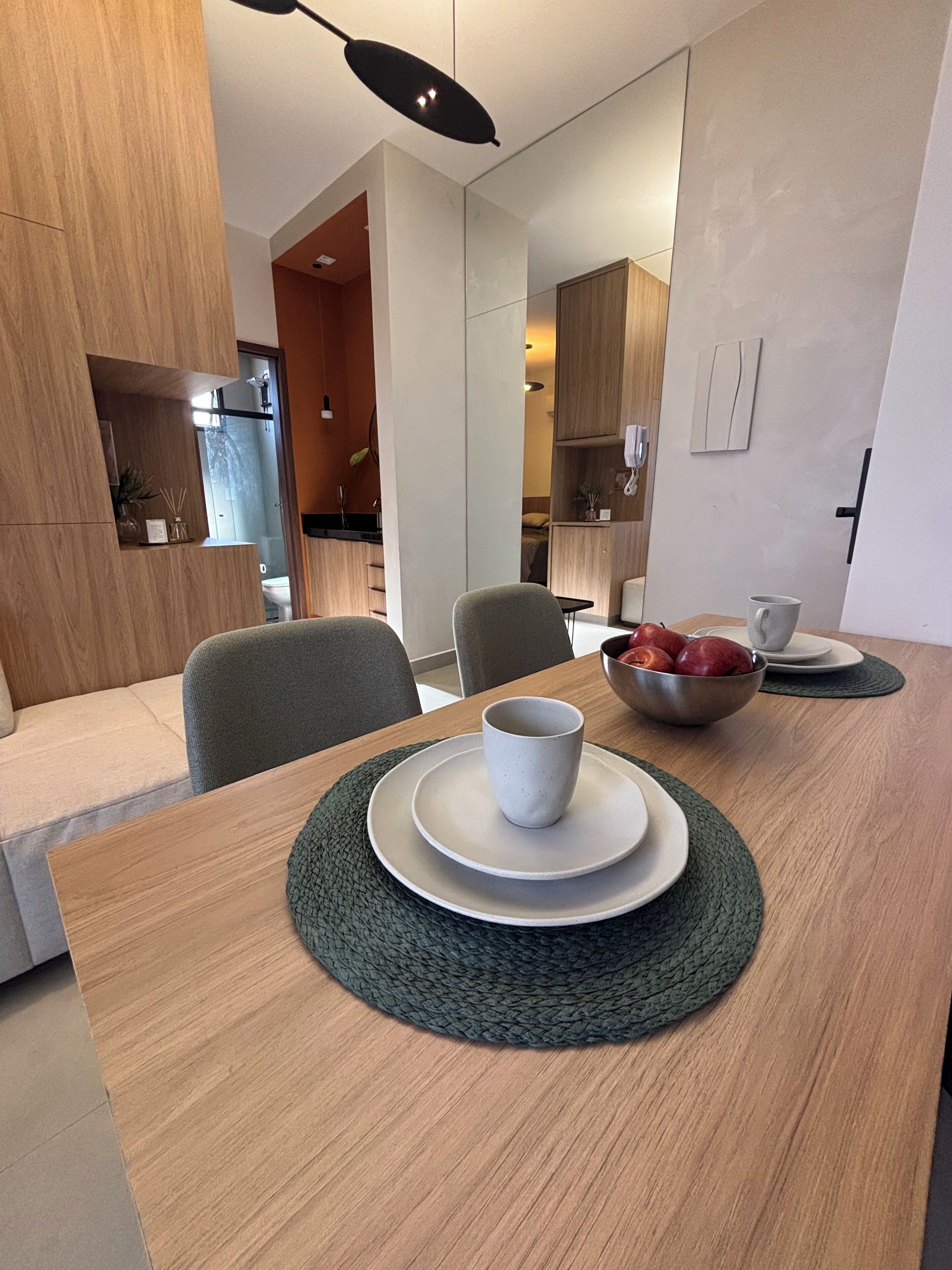 A modern dining area with a wooden table, two chairs, a bowl of fruit, and a cup on a plate.