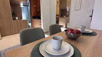 A modern dining area with a wooden table, two chairs, a bowl of fruit, and a cup on a plate.
