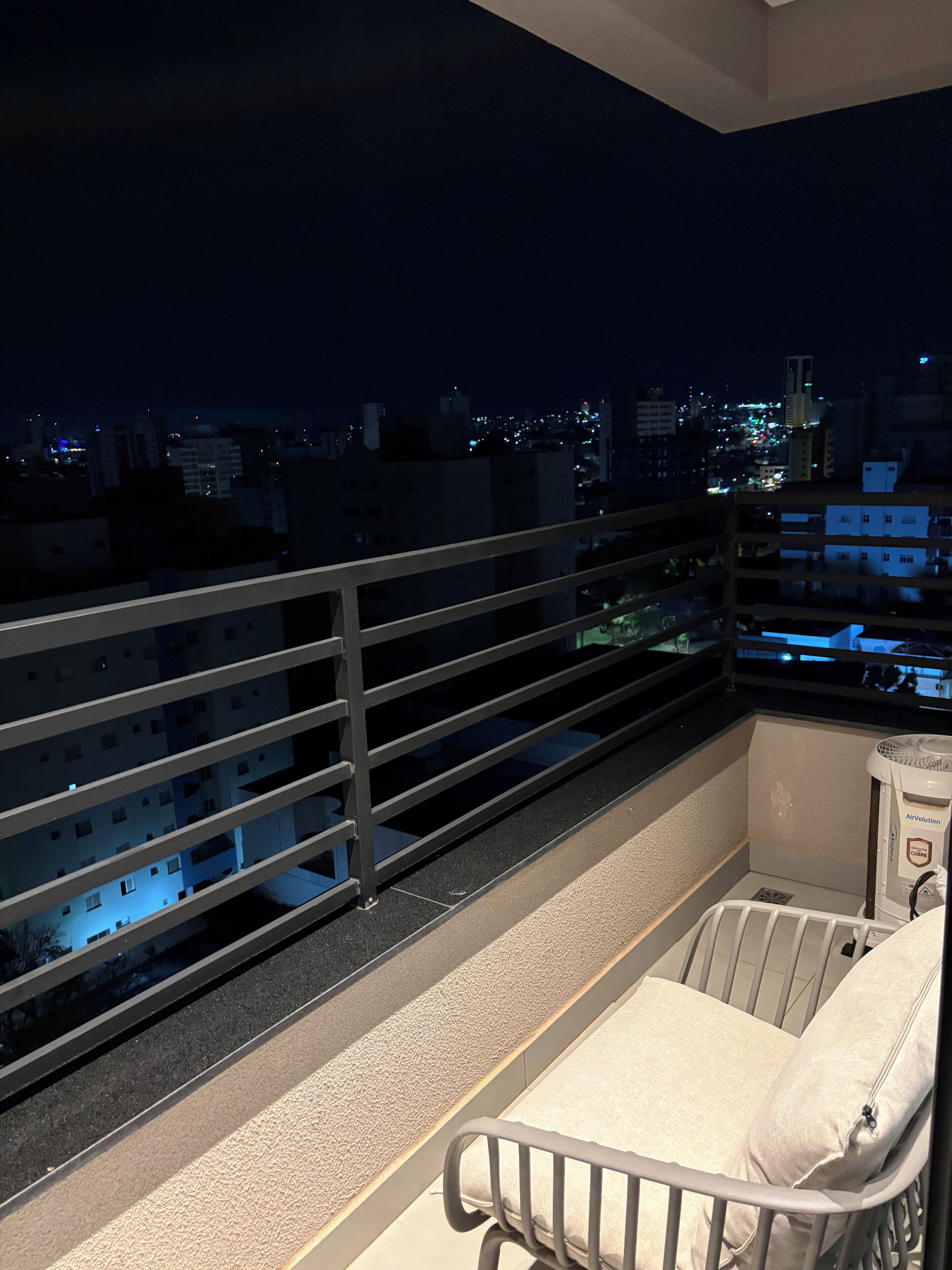 Un balcon doté d’une balustrade en métal, d’une chaise blanche avec coussin et d’une petite table sur laquelle se trouve un purificateur d’air.