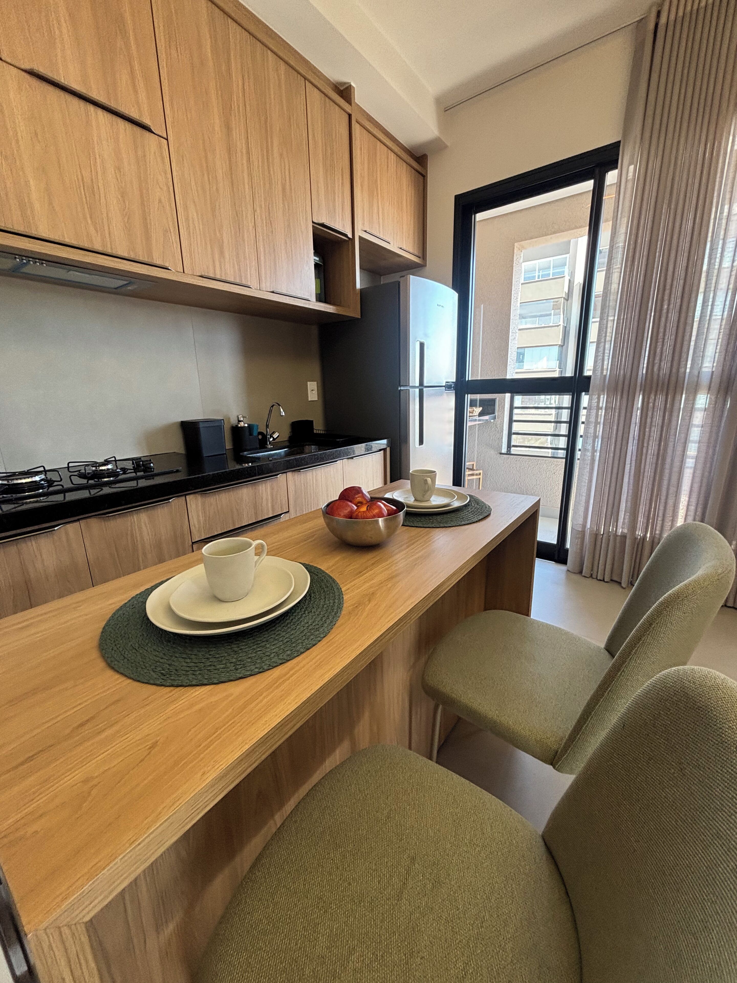 Una cocina moderna con armarios de madera, un refrigerador negro y un comedor con una mesa de madera y dos sillas.