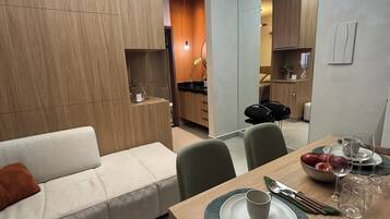 A modern living room with a sofa, dining table set with plates, glasses, and cutlery.