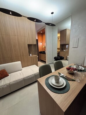 A modern living room with a sofa, dining table set with plates, glasses, and cutlery. - Monte Olympus: Apt moderno com sacada 10º andar (Uberlândia)