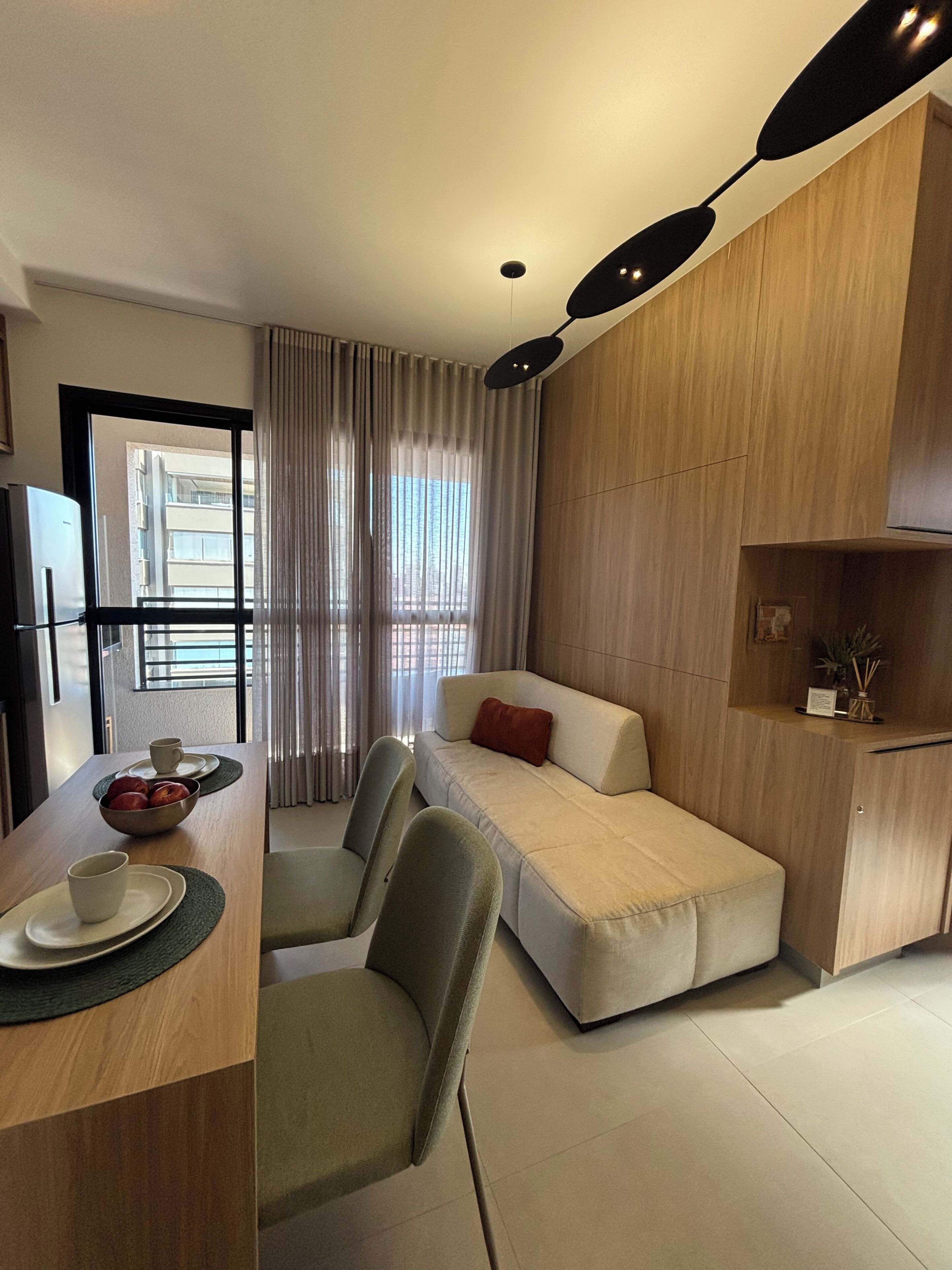 Habitación de hotel compacta con kitchenette, zona de comedor con mesa y sillas, sofá cama y un ventanal con cortinas.