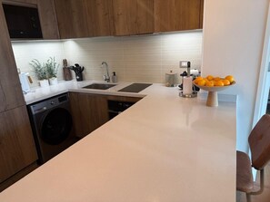 Una cocina con armarios de madera, lavadora, un lavabo y un cuenco de naranjas.