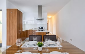 Une cuisine moderne avec des armoires blanches, une hotte en acier inoxydable et un coin repas doté d’une table en bois, mise pour quatre personnes.